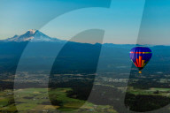 Aerial view of hot air balloon floating over farmland and Mt. Rainer in the distance.