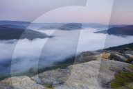 Dawn light breaks above the Peak District hills with a cloud inversion covering the Ladybower reservoir below Bamford Edge.