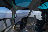 A helicopter flies towards the Himalayas as the pilot points towards the Ganesh Himal range through the window