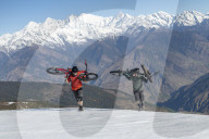 Mountain bikers carry their bikes up a snow covered slope in the Himalayas with views of the Langtang range in the distance