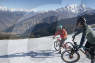 Mountain bikers descend a snow covered slope in the Himalayas with views of the Langtang range in the distance