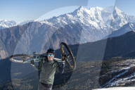 A mountain biker carries his bike up in the Himalayas with views of the Langtang range in the distance