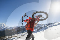 Mountain bikers carry their bikes up a snow covered hillside in the Nepal Himalayas with views of the Langtang mountain range