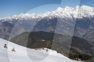 Mountain bikers cycle along a snow covered slope in the Himalayas with views of the Langtang range in the distance