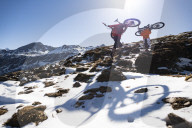 Mountain bikers carry their bikes up a snow covered hillside in the Nepal Himalayas with views of the Langtang mountain range