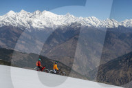 Mountain biking on a snow covered slope in the Himalayas with views of the Langtang mountain range in the distance