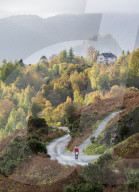 A lone cyclist on the lower slopes of Catbells with distant Castle Crag, and Manesty woods in Borrowdale, October 2018