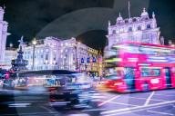 A bus and taxi zoom round Piccadilly Circus, London, England