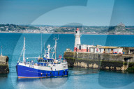 Fishing boat coming into the harbour at the village of Newly with St Michael's mount at Marazion in the distance, Cornwall, UK.