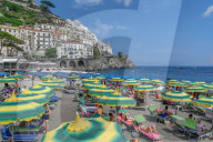 Amalfi Town, Italy daily beach view with bathers and colorful umbrellas before low rise buildings in Costiera Amalfitana.