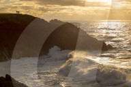 A couple enjoy the view of sunset and crashing waves.