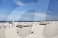 Vast beach with roofed wicker beach chairs on wooden plateaus and people celebrating the summer