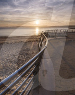 The sun sets in line with railings on the slipway at the RNLI station, Exmouth, Devon, UK