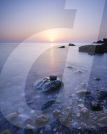 A colourful spring sunrise over Torbay with warm light glinting off the wet rocks, Anstey's Cove, Torquay, Devon, UK