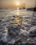 A colourful sunrise over Torbay with warm light glinting off the wave and wet rocks, Anstey's Cove, Torquay, Devon, UK