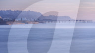 Sun making the sea wall glow on Teignmouth sea front with Teignmouth Pier behind, viewed from Shaldon, Devon, UK