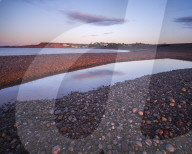First sunlight falls on Budliegh Salterton with pebbles on the curving beach from Otter Mouth, Budliegh Salterton, Devon, UK