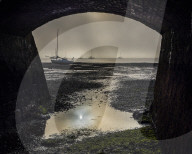 Boats on the Exe estuary in heavy fog viewed through an arch under the Exmouth to Penzance railway line, Starcross, Devon, UK