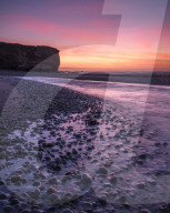 The River Otter meets the sea with strong dawn colour, wet pebbles and the cliff of Otter Head at Budliegh Salterton, Devon, UK