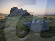 Sun behind granite rocks at Haytor in Dartmoor National Park and distant mist in the Teign Valley, Bovey Tracey, Devon UK