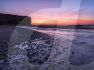 The River Otter meets the sea with strong dawn colour, wet pebbles and the cliff of Otter Head at Budliegh Salterton, Devon, UK
