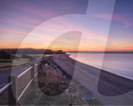 Colourful dawn with sweep of the shoreline, beach huts, pebbles and the cliff of Otter Head at Budliegh Salterton, Devon, UK