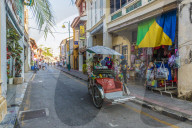 A local rickshaw tuk tuk driver in a colourful street scene in George Town, Penang Island, Malaysia, Southeast Asia, Asia.