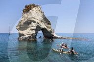 Kayakers go through arch rock formation with crystal clear water, Kleftiko, Milos, Cyclades, Aegean Sea, Greek Islands; Greece