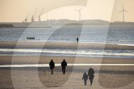 Walkers on the beach at sunset with docks of Boulogne-s-Mer behind, Wimereux, Pas-de-Calais, Hauts-de-France region, France
