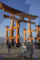 Tourists walking under the torii gate of Miyajima at low tide.