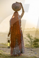 Ahir Woman in traditional colorful cloth carrying water in a clay jug on her head, Great Rann of Kutch Desert, Gujarat, India