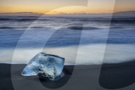 Glacier ice on black sand beach with waves washing up the beach on a winter day, near Jokulsarlon, South Iceland