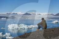 Young male sat admiring the view of Jokulsarlon Glacier Lagoon , South East Iceland, Iceland