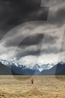 Man in red coat stood looking at snow capped mountains, Fiordland National Park, New Zealand