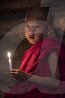 A young monk sat holding candle at temple, Bagan (Pagan), Myanmar (Burma), Asia