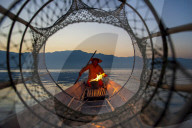 Intha leg rowing fisherman viewed through net on Inle Lake., Shan State, Myanmar