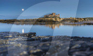 Moonlit Bamburgh Castle reflected in still water at dusk, Bamburgh, Northumberland, England.