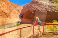 Tourist woman with wide hat standing at balcony and admires Mutitjulu Waterhole at the end of short Kuniya walk in Uluru-Kata Tjuta National Park. Tourism in Northern Territory, Central Australia.