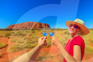 Lifestyle woman doing cheers to celebrate at Uluru Ayers Rock at sunset in Uluru-Kata Tjuta National Park. Blonde traveler in Australian outback Red Centre. Tourism in Northern Territory, Australia.