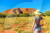 Tourism in Northern Territory, Central Australia. Lifestyle tourist woman in hat looks Uluru Ayers Rock in Uluru-Kata Tjuta National Park. Caucasian traveler in Australian outback in dry season.