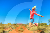 Happy tourist woman jumping at Uluru Ayers Rock in Uluru-Kata Tjuta National Park. Lifestyle traveler enjoying in Australian outback Red Centre. Tourism in Northern Territory, Central Australia.