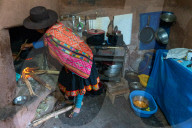 Local woman in colourful traditional dress cooks breakfast over an open fire, Chumbe Community, Lamay, Sacred Valley, Peru