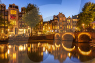 Illuminated canal bridge with reflections at night over the Singel Torensluis canal Amsterdam Holland Netherlands EU Europe