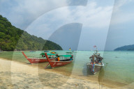 Three long tailed boats on a sandy beach.