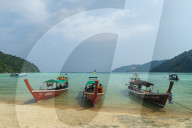Three long tailed boats on a sandy beach.