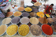Woman in red sari at village street market stall selling spices, seeds and pasta, Chhota Udepur, Gujarat