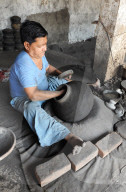 Man beating hand made charcoal dusted terracotta water jar into traditional shape with a wooden paddle, Chhote Udepur, Gujarat