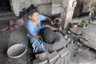 Man beating hand made charcoal dusted terracotta water jar into traditional shape with a wooden paddle, Chhote Udepur, Gujarat