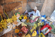 Man preparing puja offerings from flowers, coconuts and fruit in 11th century Brihadisvara temple, Thanjavur, Tamil Nadu