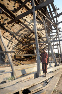 Boatbuilder beneath the hull of ocean going dhow under construction by hand from Sal wood, Rukmavati River, Mandvi, Gujarat